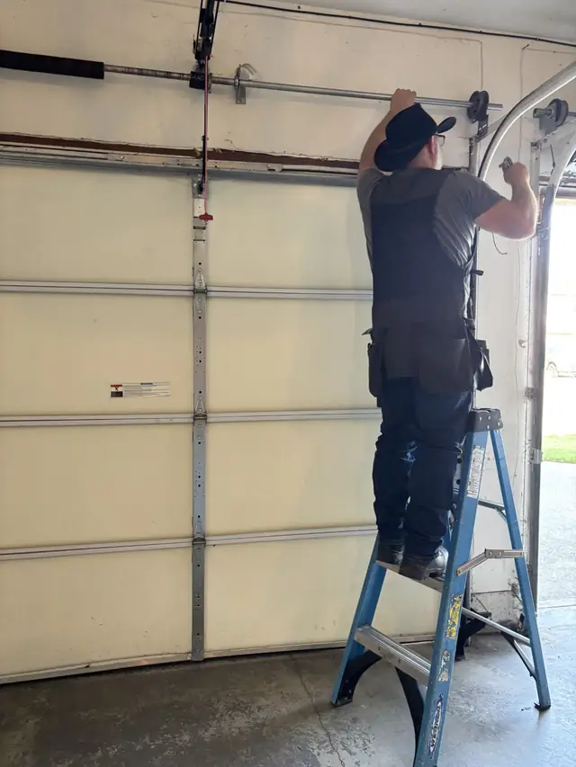 Dave working on garage door track and opener hardware from a ladder inside a garage